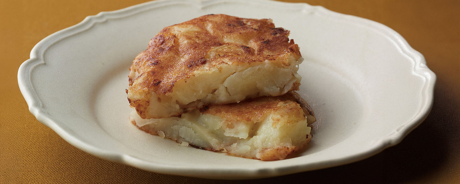 Golden, crispy potato frico stacked on a plate, showing a soft, melted interior.