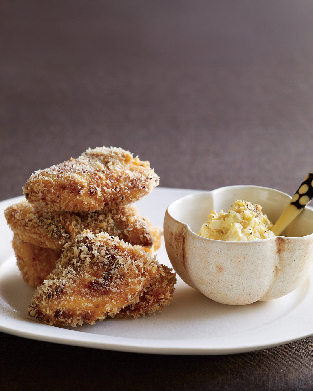 Crispy breaded salmon pieces stacked on a plate with a small bowl of creamy tartar sauce.