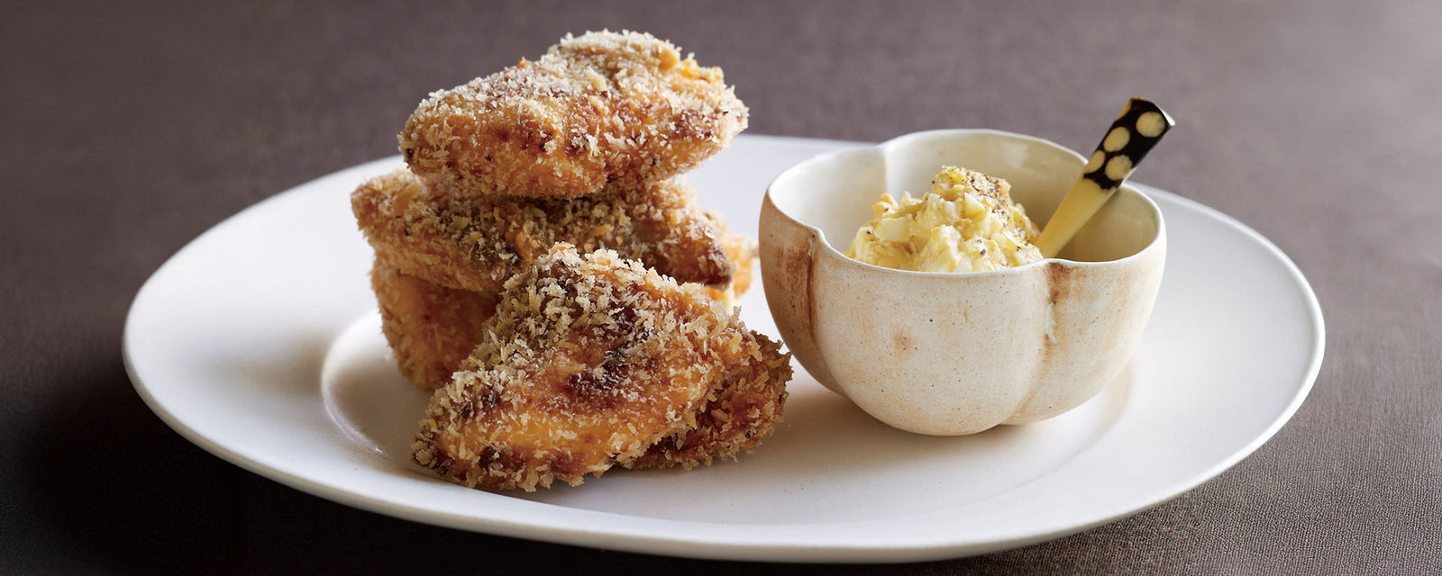Crispy breaded salmon pieces stacked on a plate with a small bowl of creamy tartar sauce.