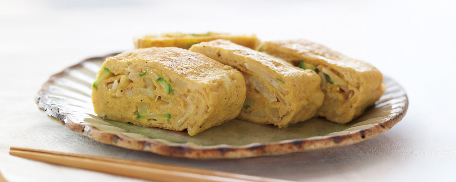 Japanese rolled omelette filled with potato and asparagus slices on a ceramic plate