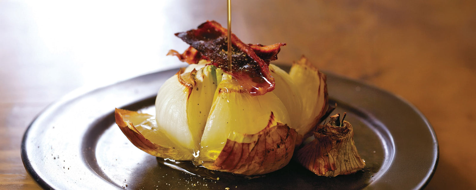 Whole roasted spring sweet onions topped with crispy bacon and drizzled with oil on a plate
