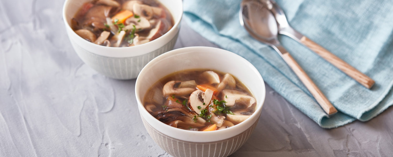 Mushroom soup with sliced mushrooms, carrots, and herbs in a clear broth