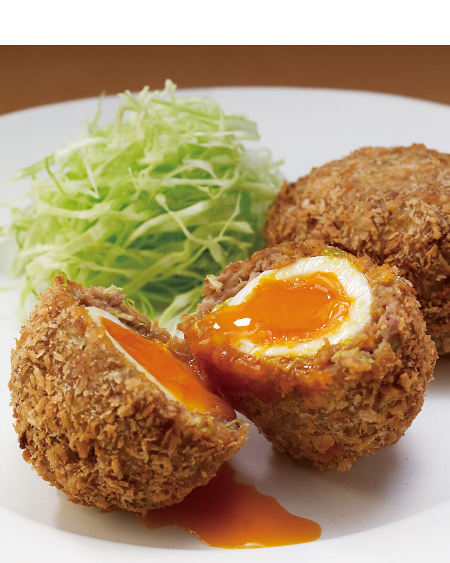 A golden-brown, deep-fried Scotch Egg served on a plate with shredded cabbage.