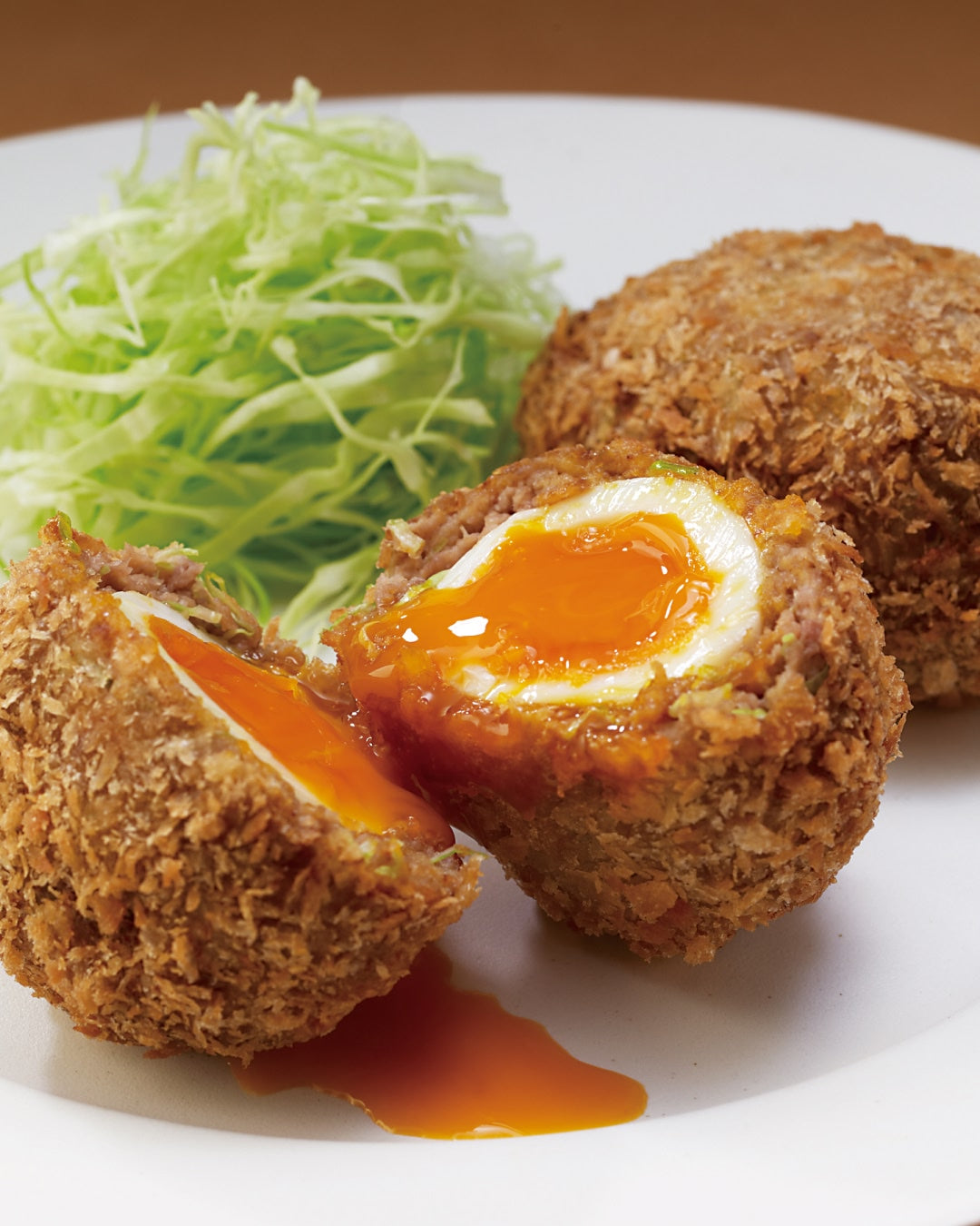 A golden-brown, deep-fried Scotch Egg served on a plate with shredded cabbage.