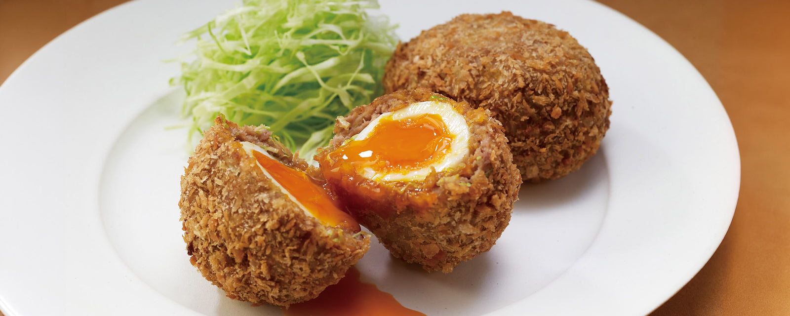 A golden-brown, deep-fried Scotch Egg served on a plate with shredded cabbage.