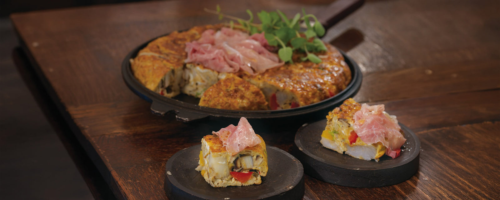 A colorful, large omelet filled with assorted vegetables, topped with thin slices of prosciutto and fresh herbs.