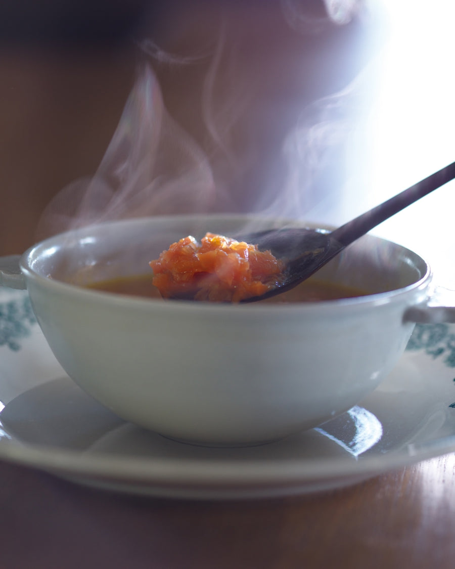A white bowl filled with chunky carrot soup, garnished with a piece of crispy bacon.