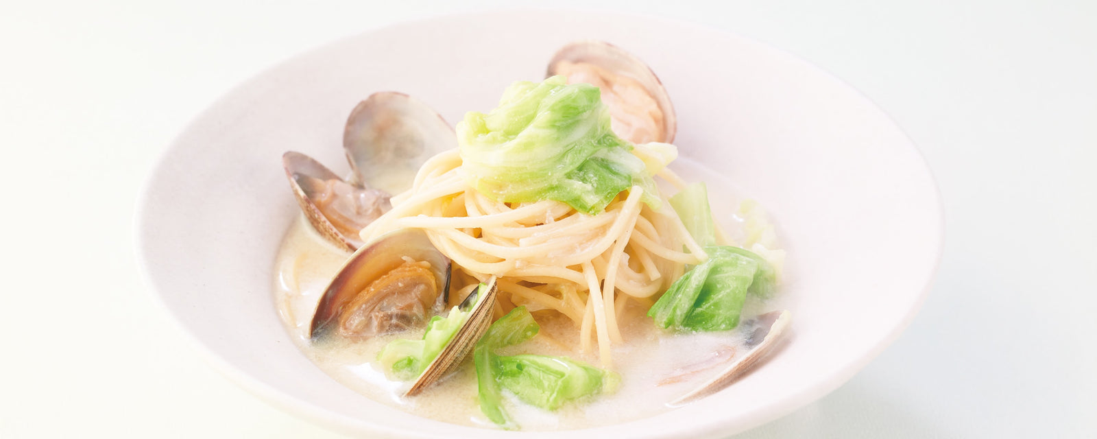 Spring creamy pasta with clams and cabbage in a soy milk sauce, served in a ceramic bowl.