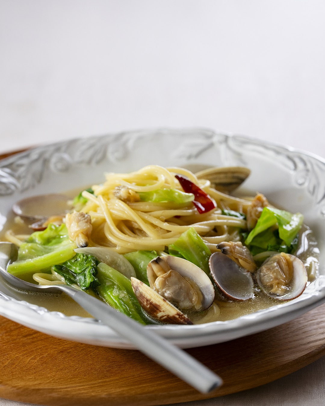 Japanese-style soup pasta with clams and bright green cabbage in a shallow white bowl.
