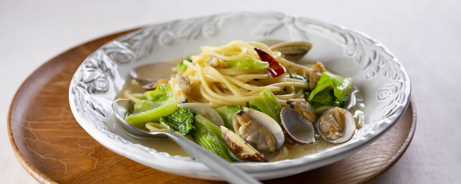 Japanese-style soup pasta with clams and bright green cabbage in a shallow white bowl.