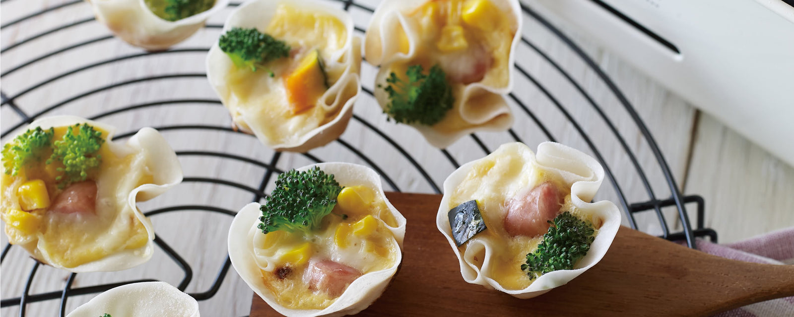 Bite-sized vegetable quiches in crispy gyoza skin shells on a wire cooling rack.
