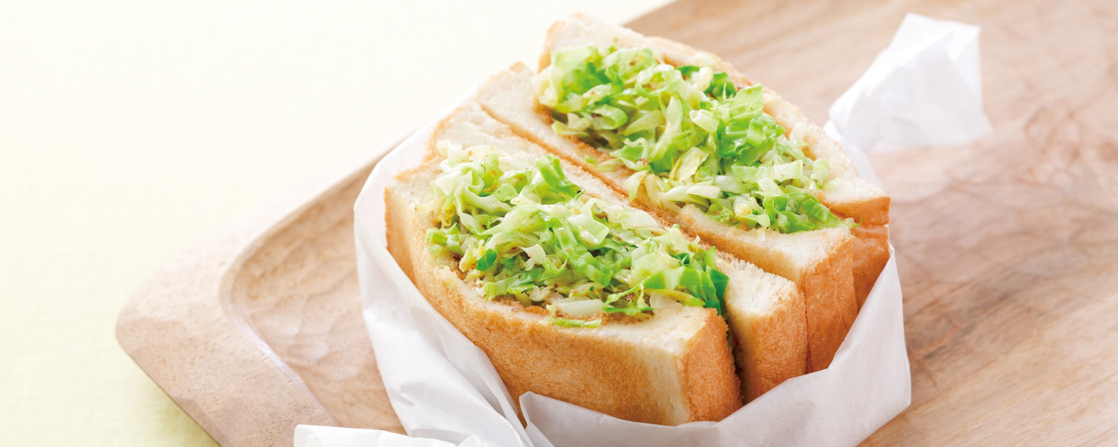 Cabbage sandwich with sautéed cabbage and butter on soft white bread, wrapped in paper and placed on a wooden board.