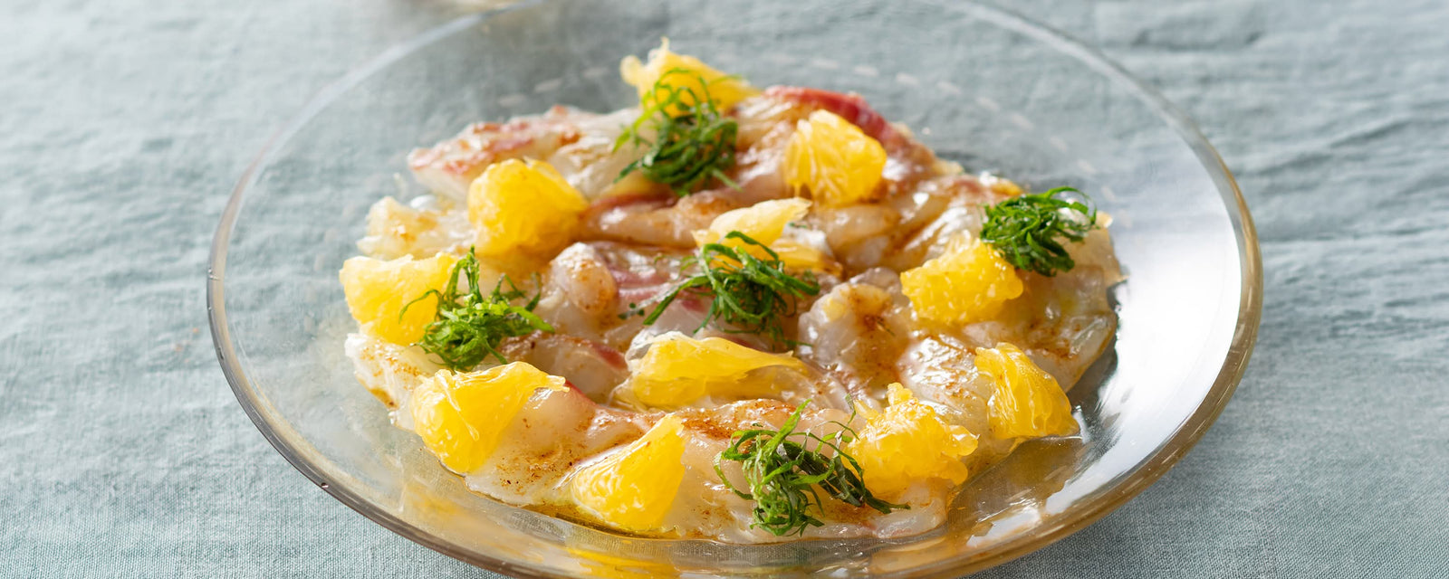 White fish carpaccio topped with Amanatsu orange segments, shiso leaves, and dashi-infused olive oil