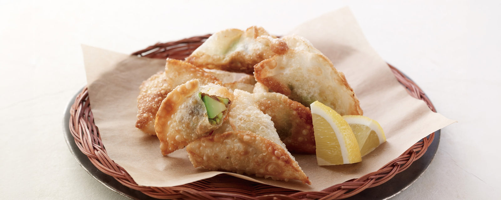 Crispy avocado samosas served with lemon wedges on a woven platter