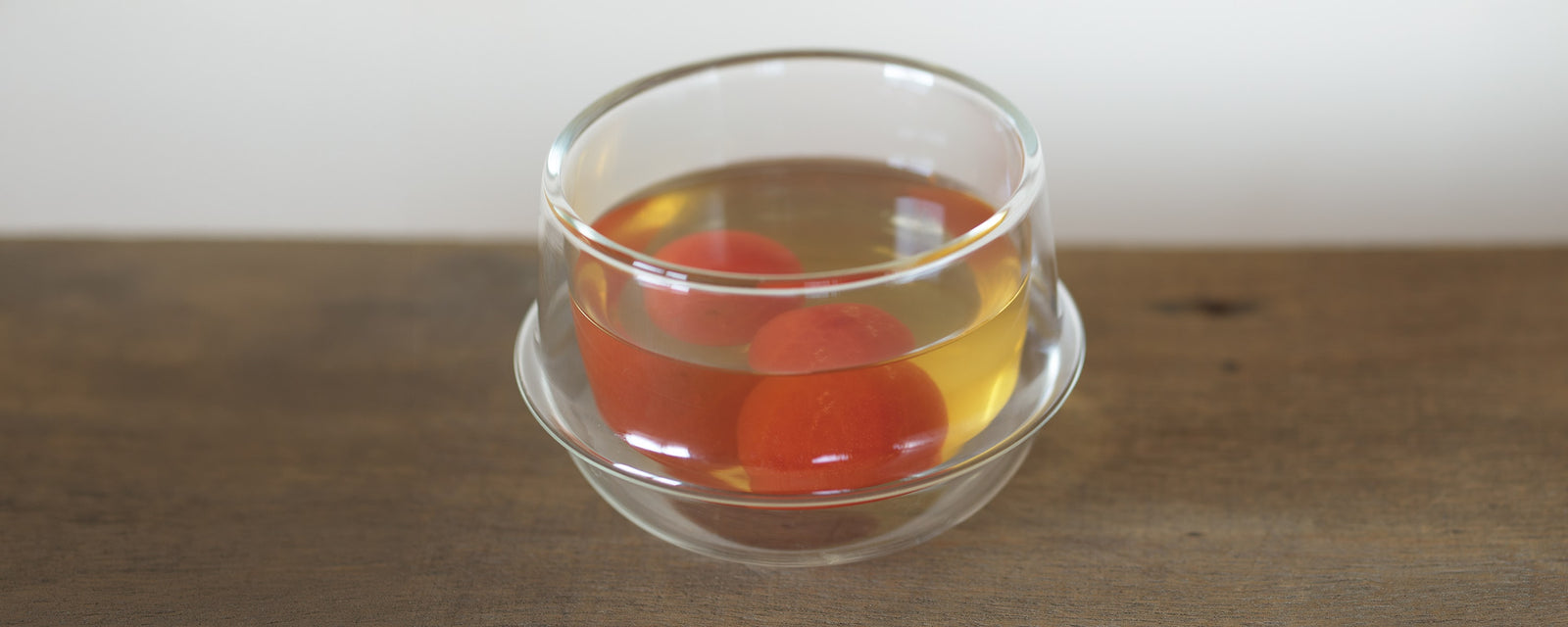 Chilled tomato dashi soup with peeled cherry tomatoes served in a clear glass bowl