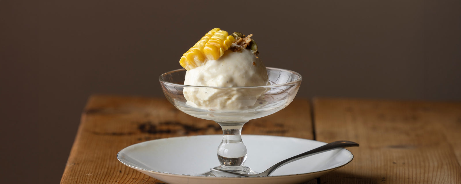 A scoop of creamy Dashi Ice Cream topped with corn and served in a glass dessert dish.