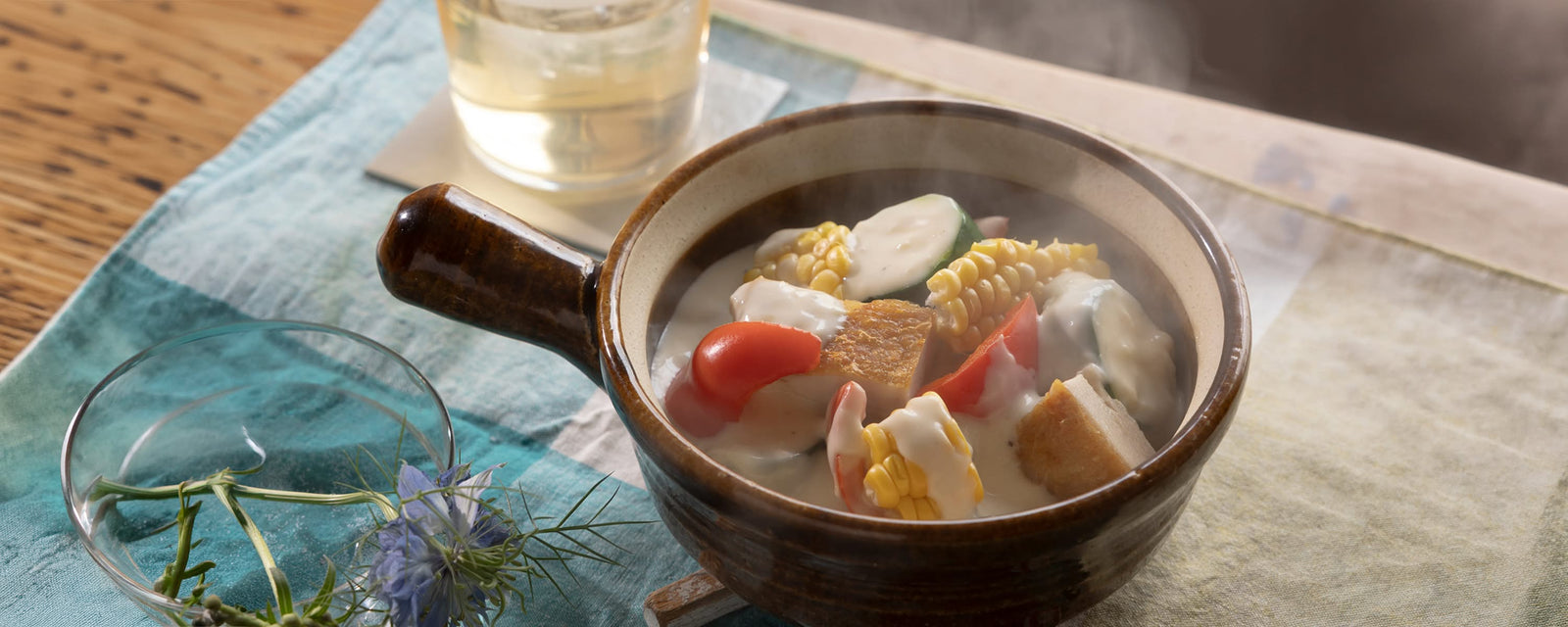 A steaming bowl of creamy chicken with corn, zucchini, cherry tomatoes, and red bell pepper in a light cream sauce.