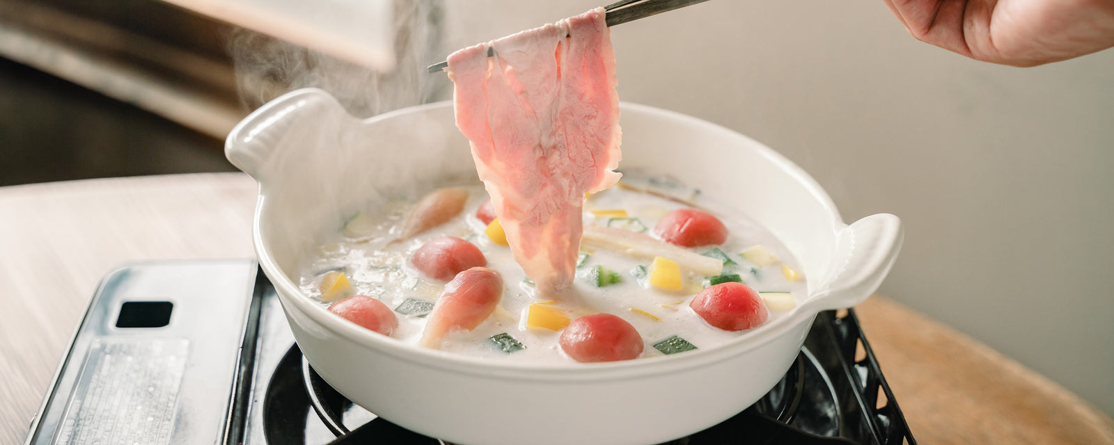 Thinly sliced beef in a creamy Corn Dashi shabu-shabu hot pot with colorful summer vegetables.