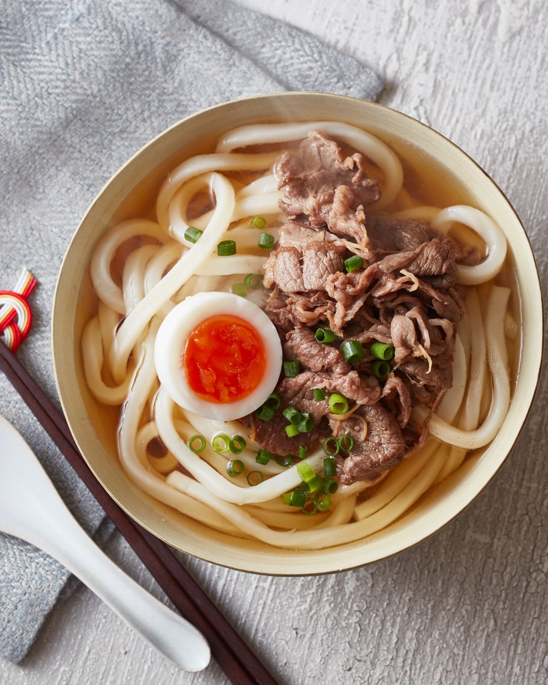 Udon noodle soup topped with sliced beef, a soft-boiled egg, and chopped green onions