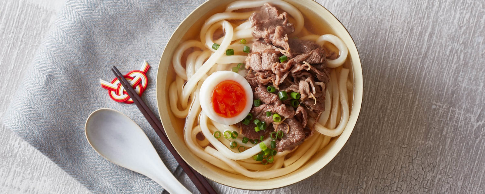 Udon noodle soup topped with sliced beef, a soft-boiled egg, and chopped green onions