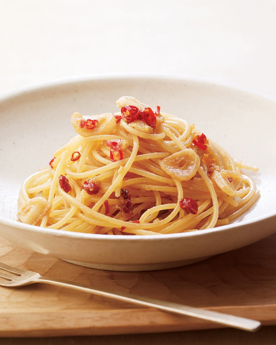 Spaghetti with garlic slices and red chili flakes served in a white bowl