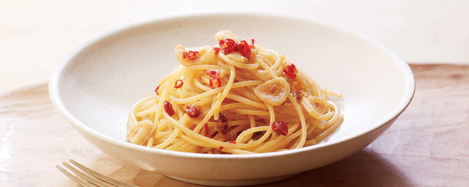 Spaghetti with garlic slices and red chili flakes served in a white bowl