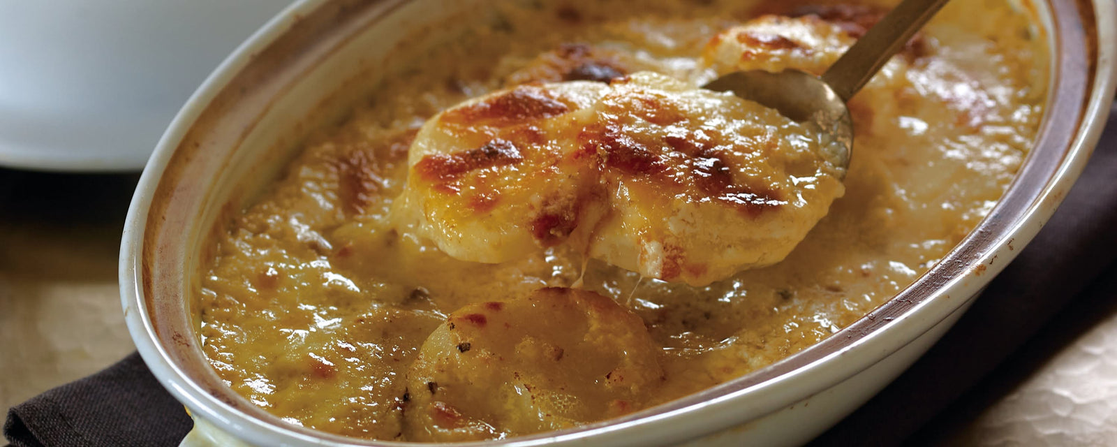 Baked cheesy potato gratin with a golden browned top being scooped from a casserole dish