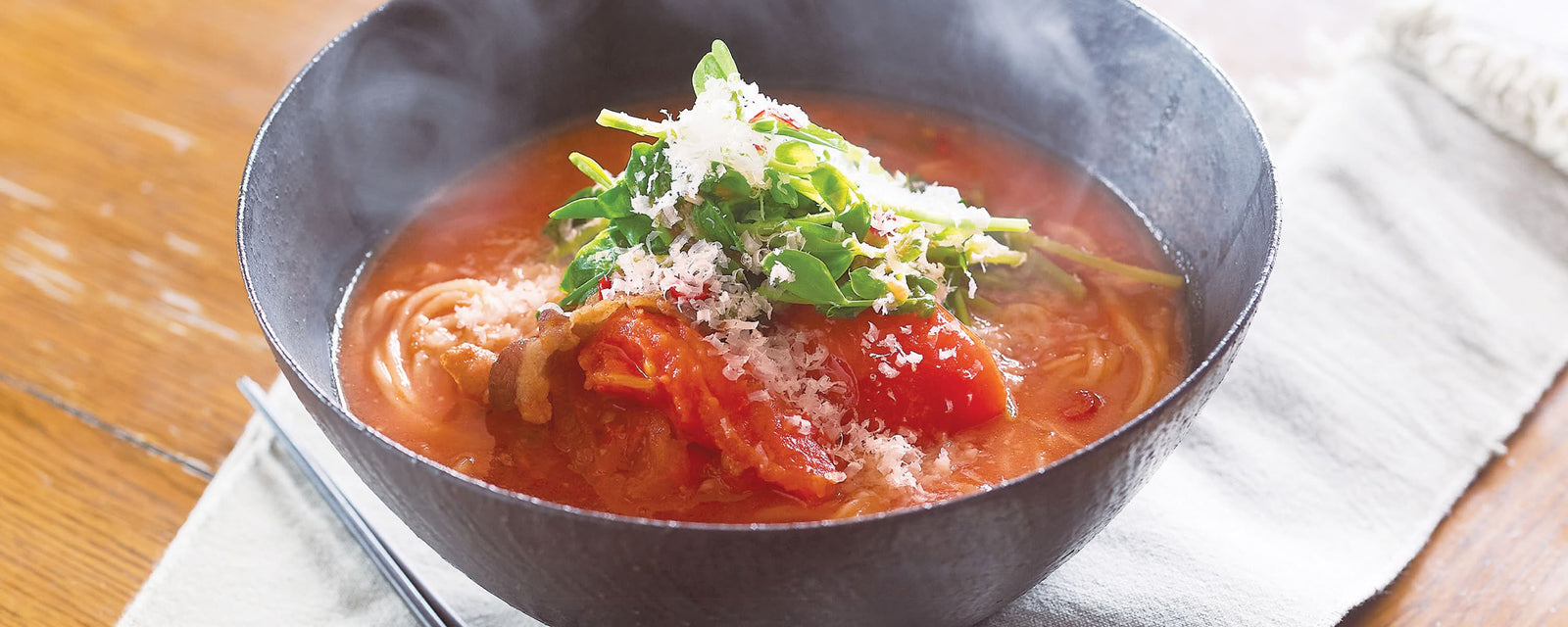 Ramen in a tomato-based soup topped with grated cheese and fresh greens