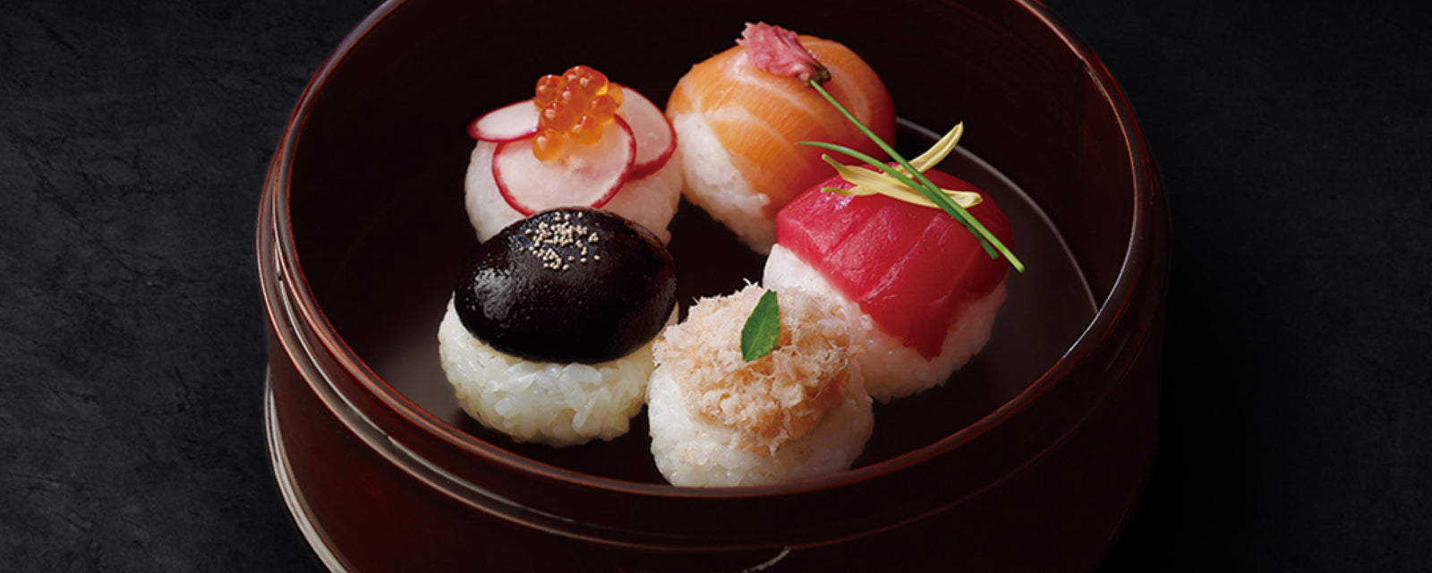 Assorted decorative temari sushi with salmon, tuna, ikura, shiitake, and radish toppings in a lacquer bowl