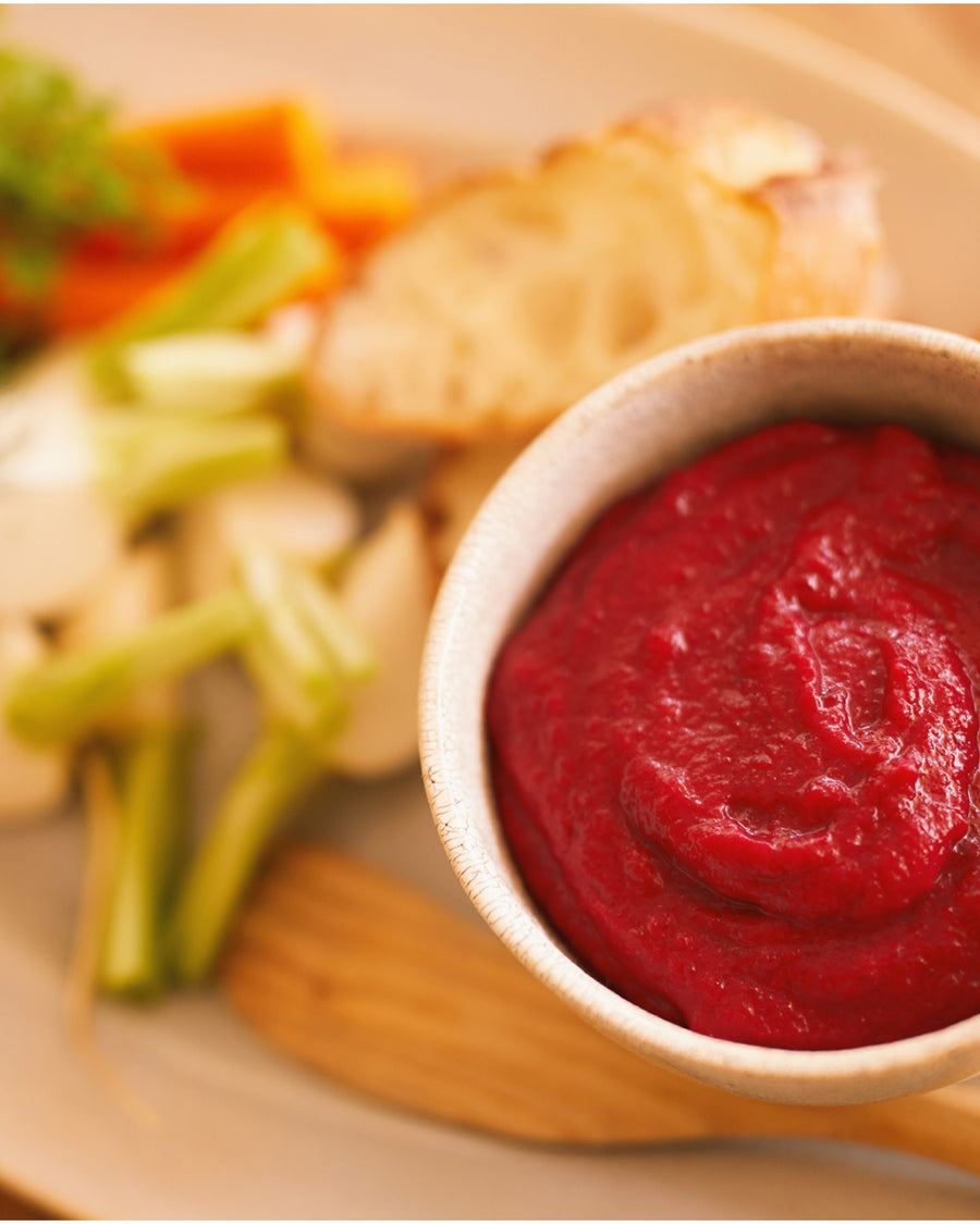 A bright red beet purée served in a bowl, garnished with fresh raw vegetables on the side.