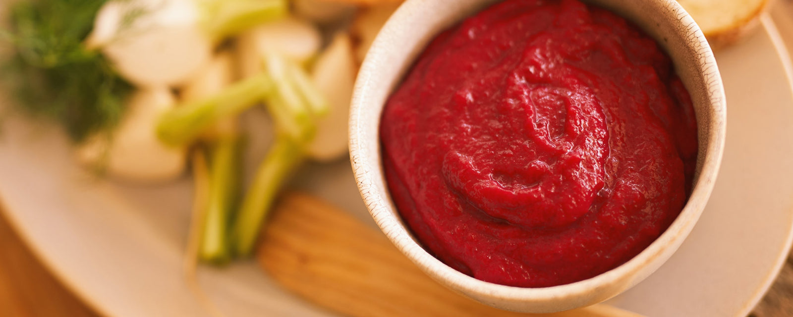 A bright red beet purée served in a bowl, garnished with fresh raw vegetables on the side.