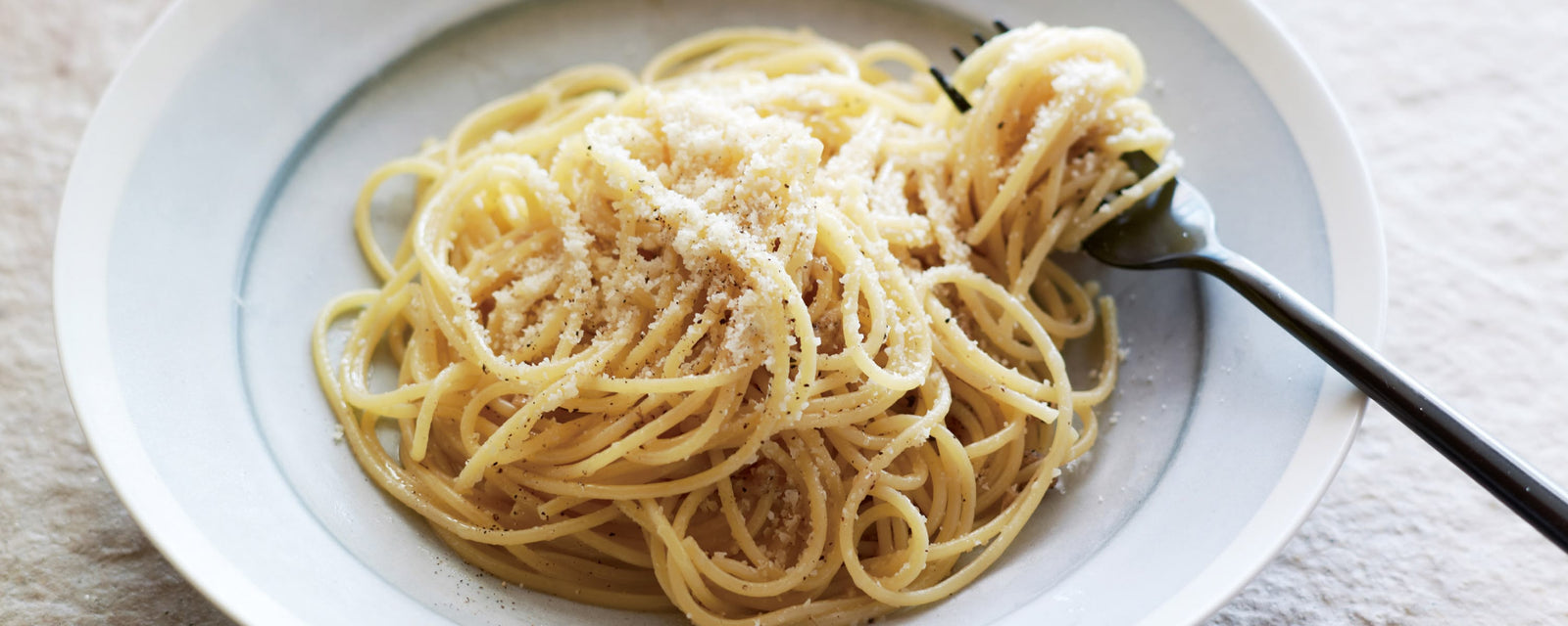 Spaghetti aglio e olio topped with grated cheese and black pepper, twirled on a fork in a simple plate