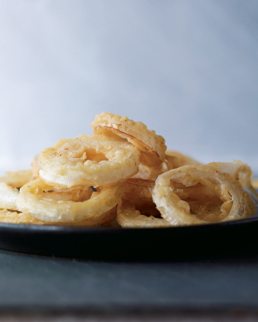 Crispy fried onion rings stacked on a plate, golden and lightly battered