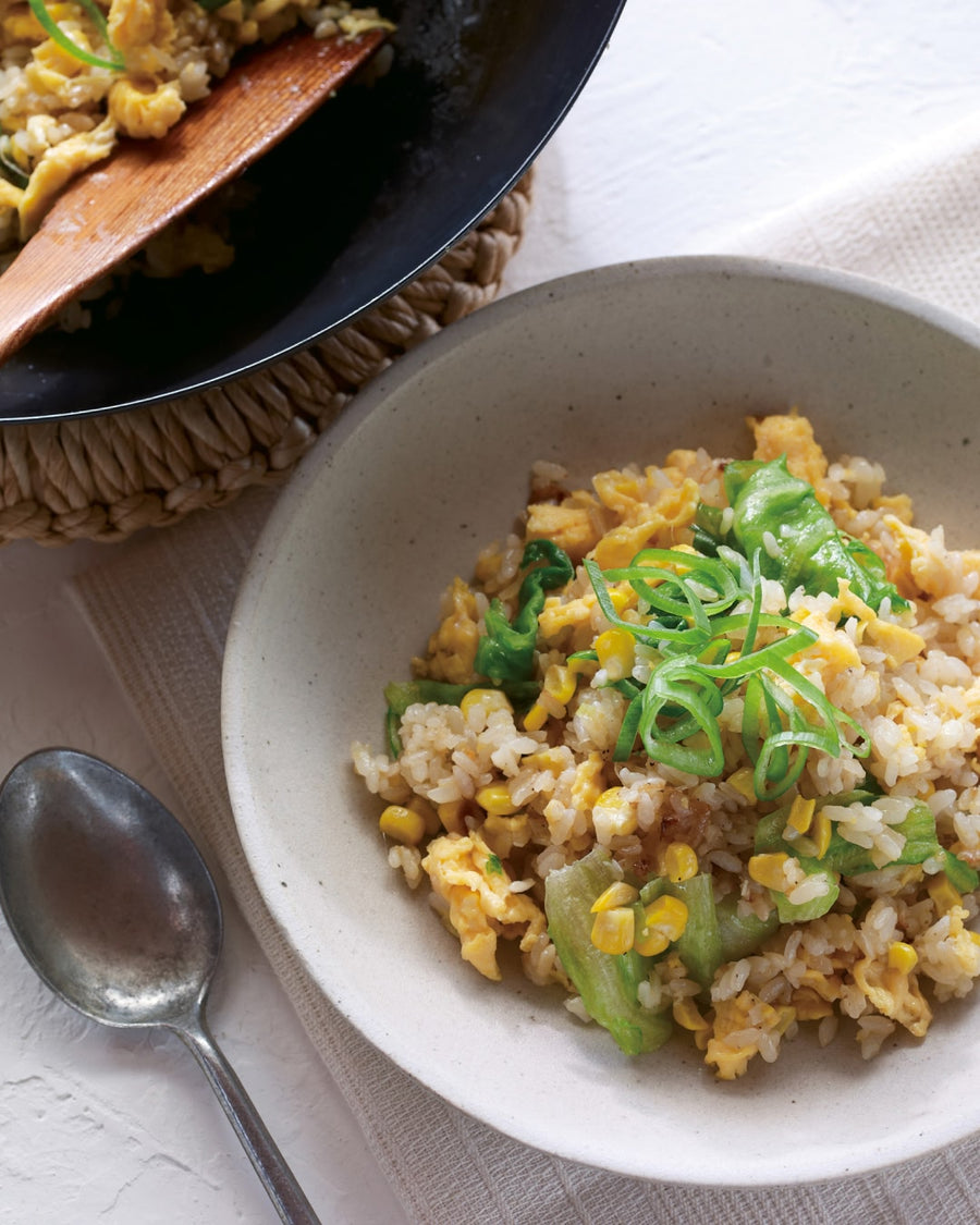 Fried rice with egg, corn, and green vegetables, garnished with sliced green onions in a ceramic bowl