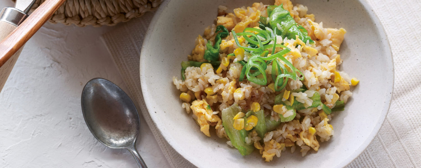 Fried rice with egg, corn, and green vegetables, garnished with sliced green onions in a ceramic bowl
