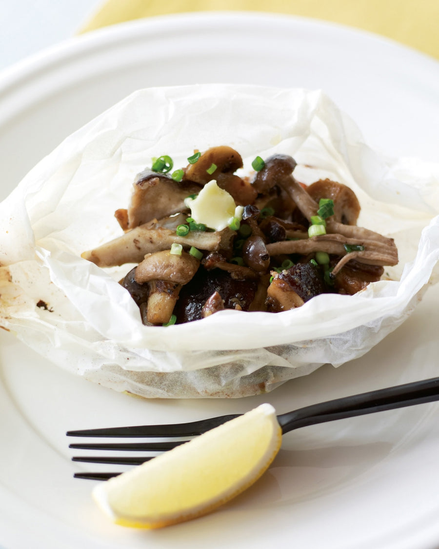 Steamed mushrooms in parchment paper, topped with butter and chopped green onions on a white plate