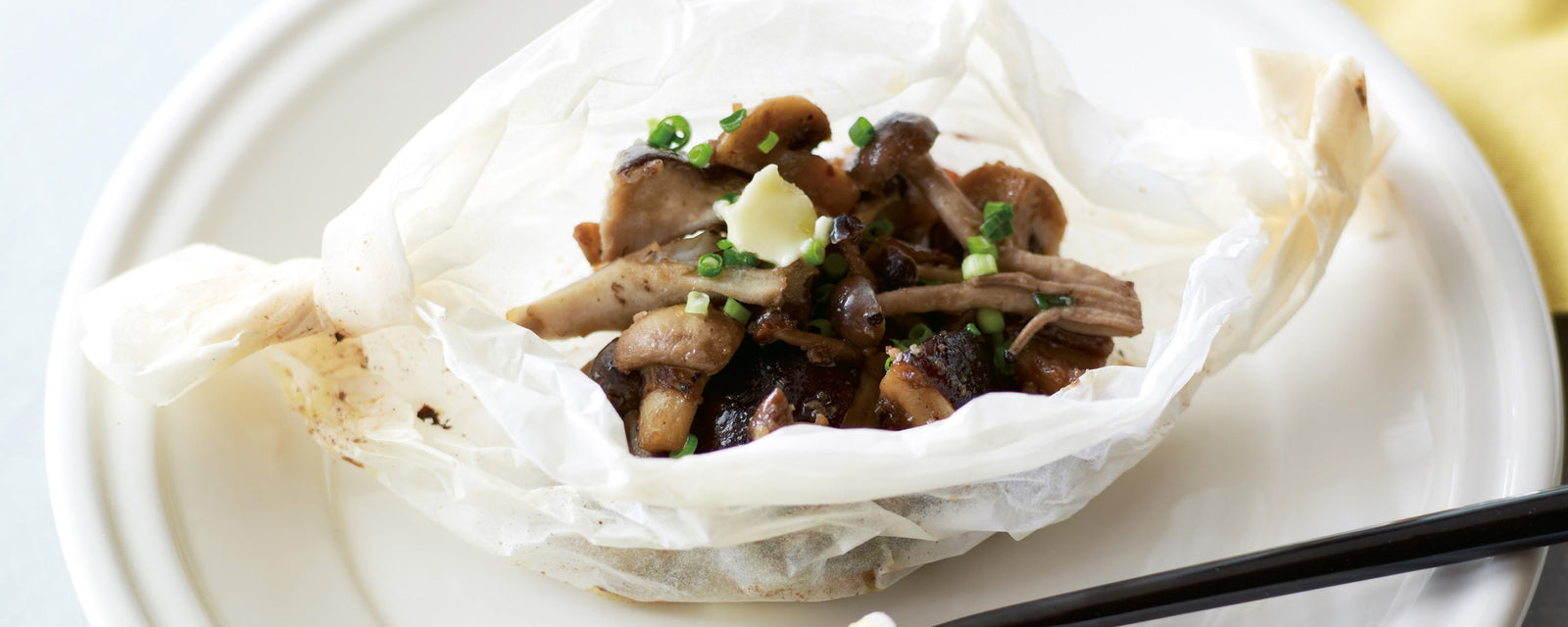 Steamed mushrooms in parchment paper, topped with butter and chopped green onions on a white plate