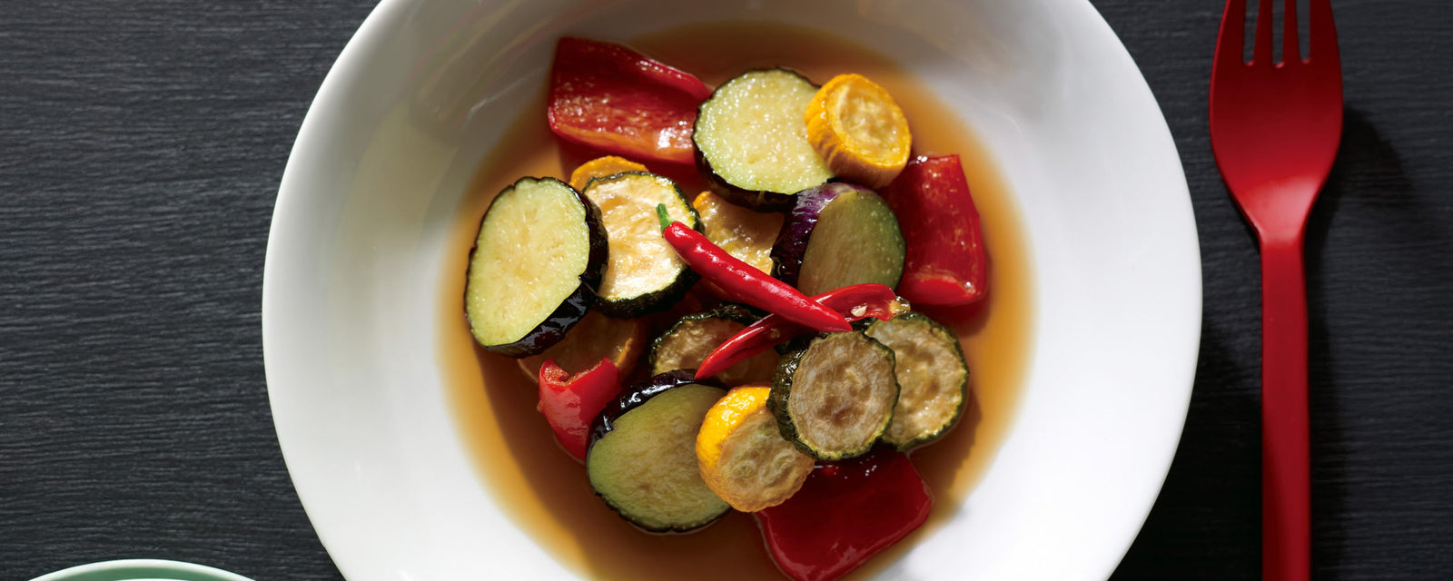 Marinated zucchini and bell peppers in a light broth, topped with red chili peppers and served in a white bowl