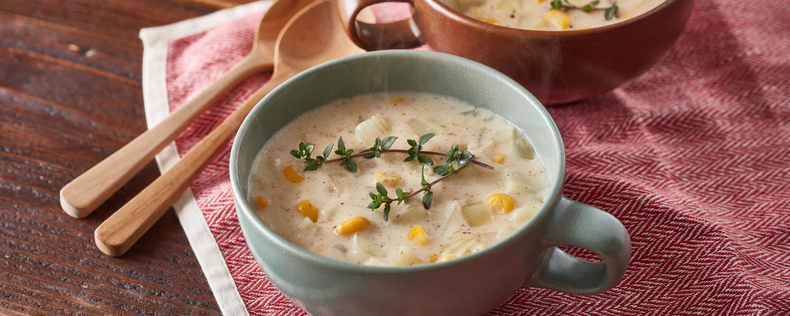 Creamy corn and potato chowder garnished with fresh herbs, served in a ceramic cup with a wooden spoon