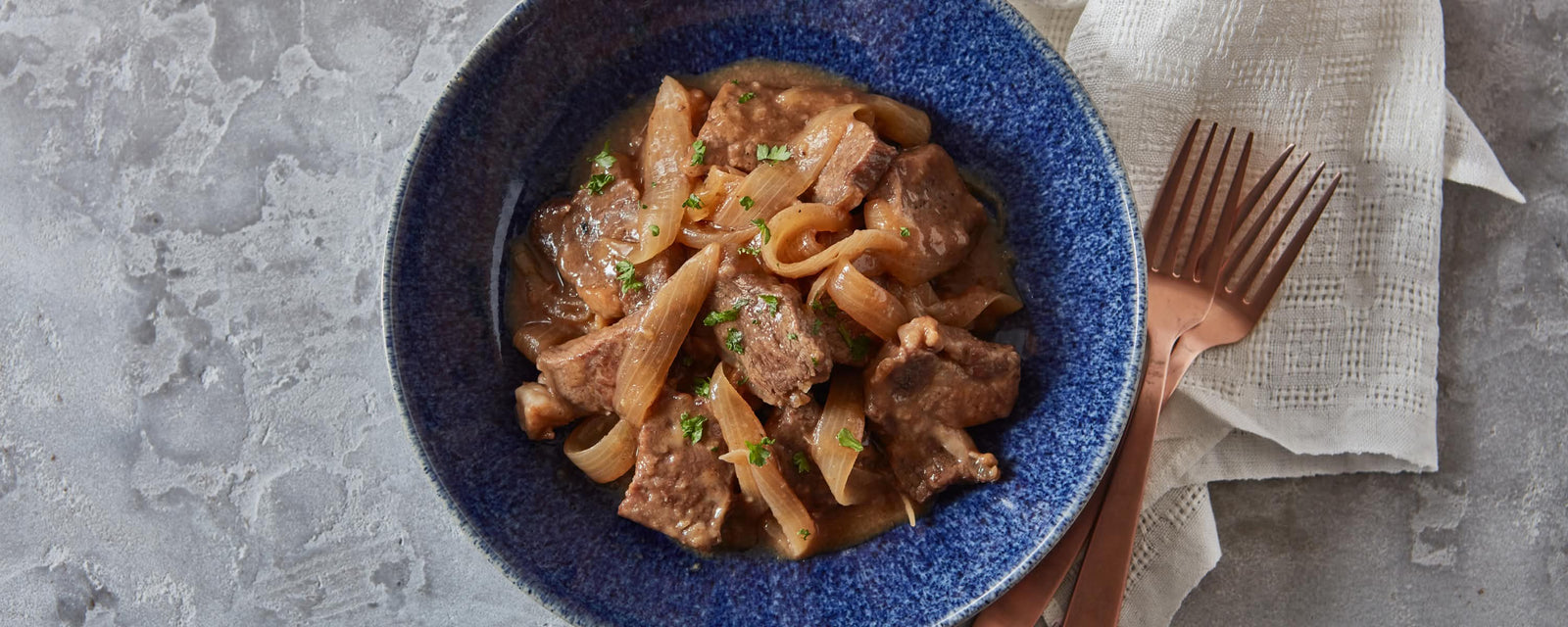 Braised beef and onions simmered in a savory dashi-based sauce, garnished with herbs and served in a deep blue bowl