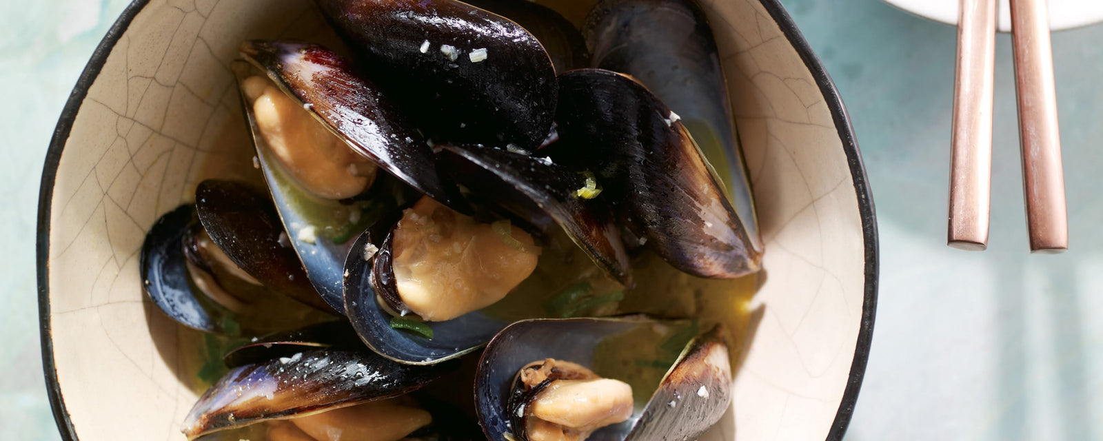 Steamed mussels in a light dashi broth with garlic and herbs, served in a rustic bowl