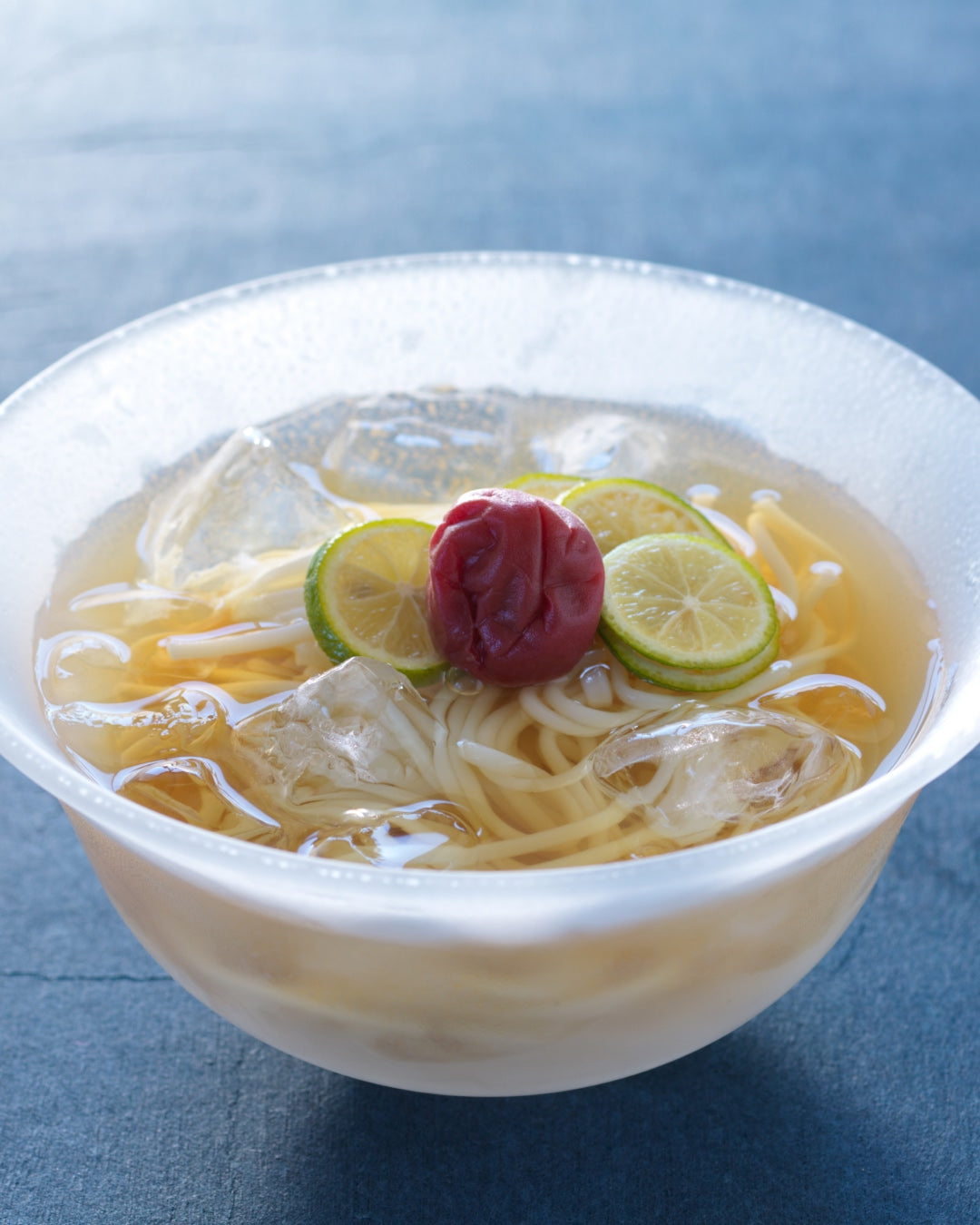 Chilled dashi udon noodles with ice, topped with ume plum and thin slices of citrus in a clear refreshing broth