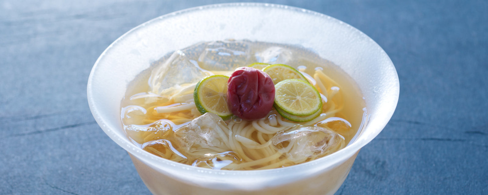 Chilled dashi udon noodles with ice, topped with ume plum and thin slices of citrus in a clear refreshing broth