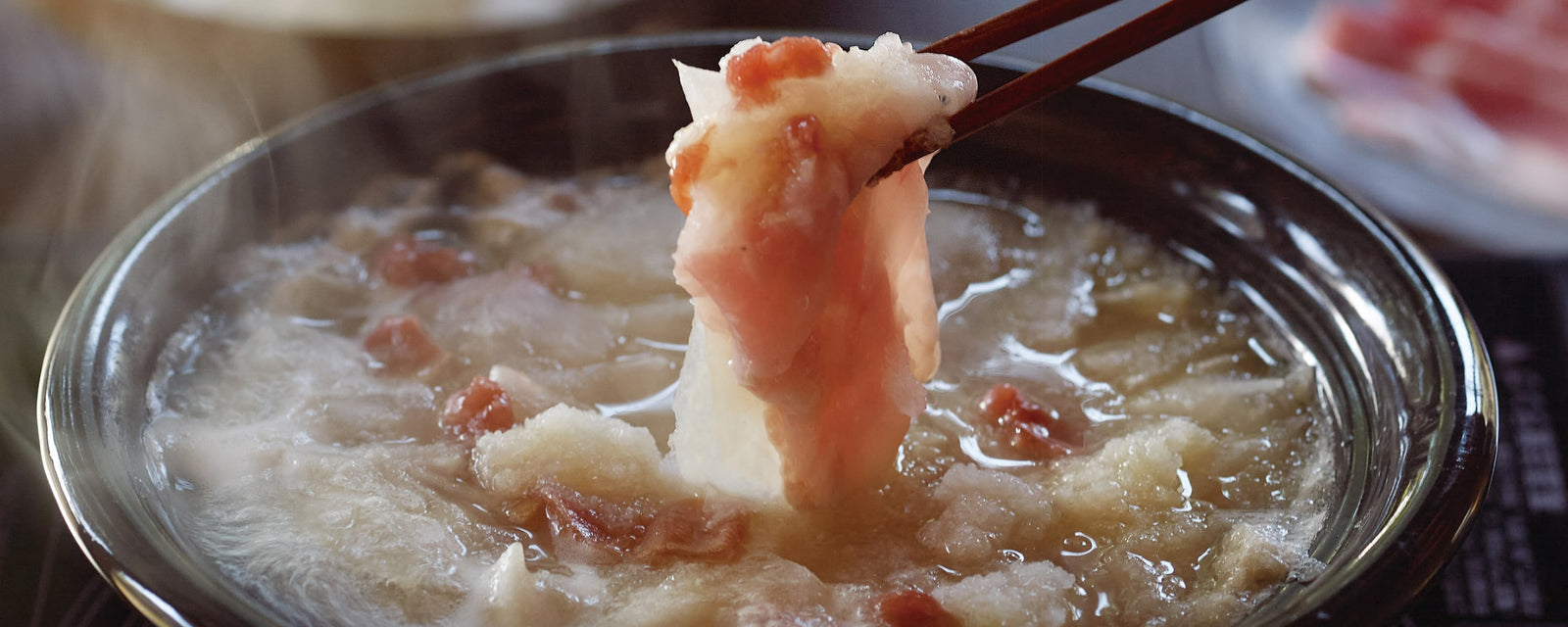 Daikon radish and thinly sliced pork lifted with chopsticks from a steaming shabu-shabu hot pot in savory dashi broth with grated daikon