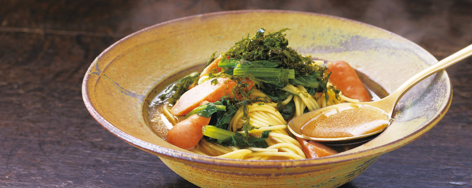 Spaghetti in rich umami dashi broth with sausages and spinach, topped with shredded nori and served with a spoon