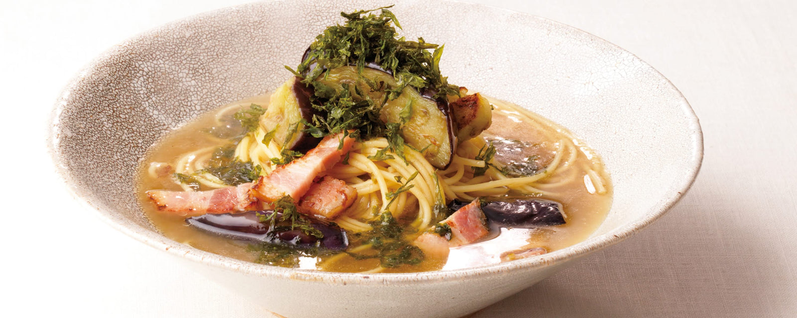 Spaghetti in savory umami dashi broth with eggplant and bacon, topped with shredded nori