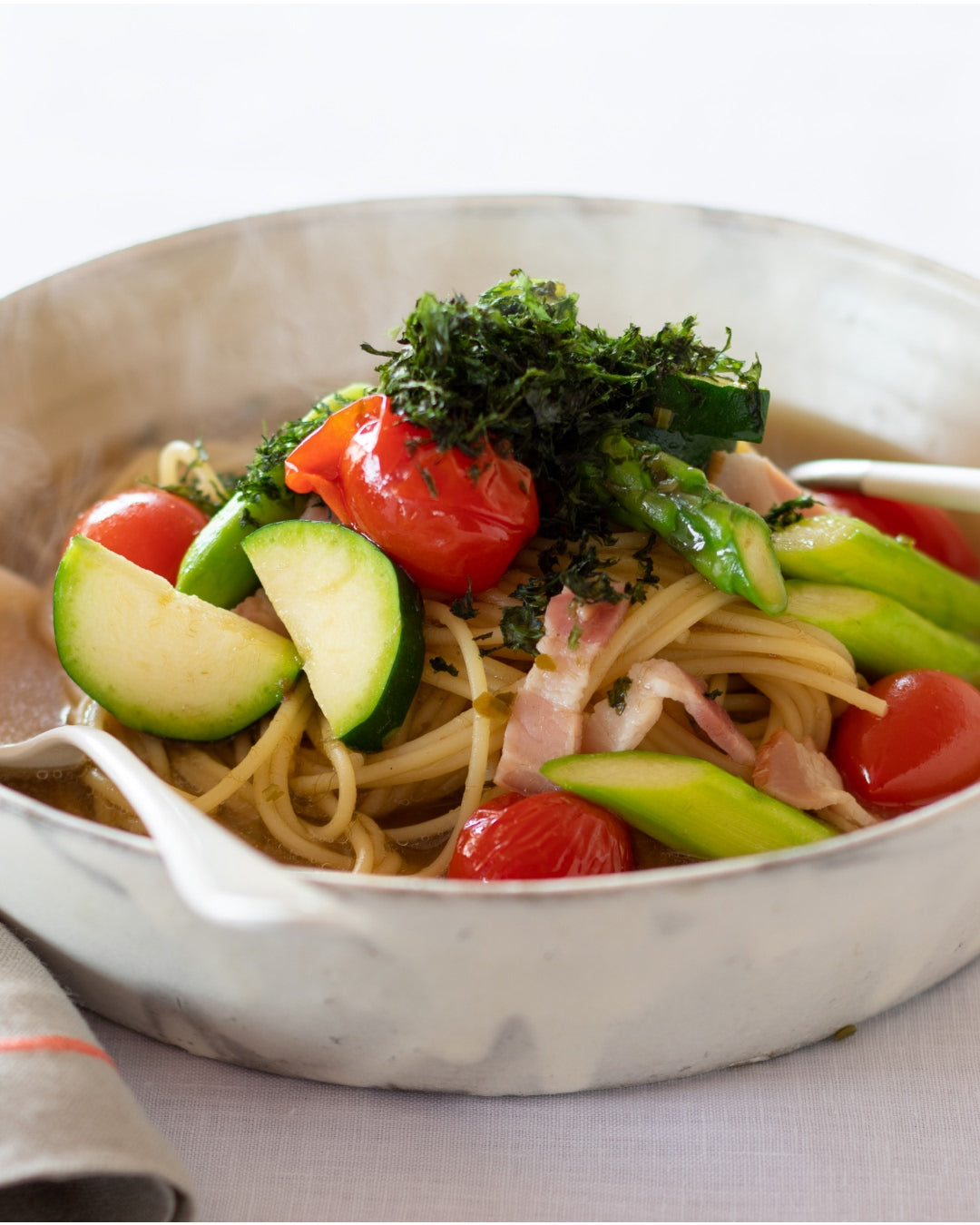 Spaghetti in light umami dashi broth with zucchini, asparagus, cherry tomatoes, and bacon, topped with shredded nori