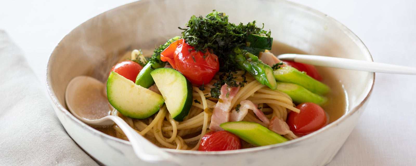 Spaghetti in light umami dashi broth with zucchini, asparagus, cherry tomatoes, and bacon, topped with shredded nori