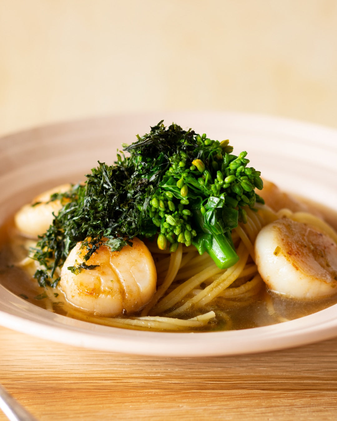 Spaghetti in light umami dashi broth topped with seared scallops, canola flower, and shredded nori