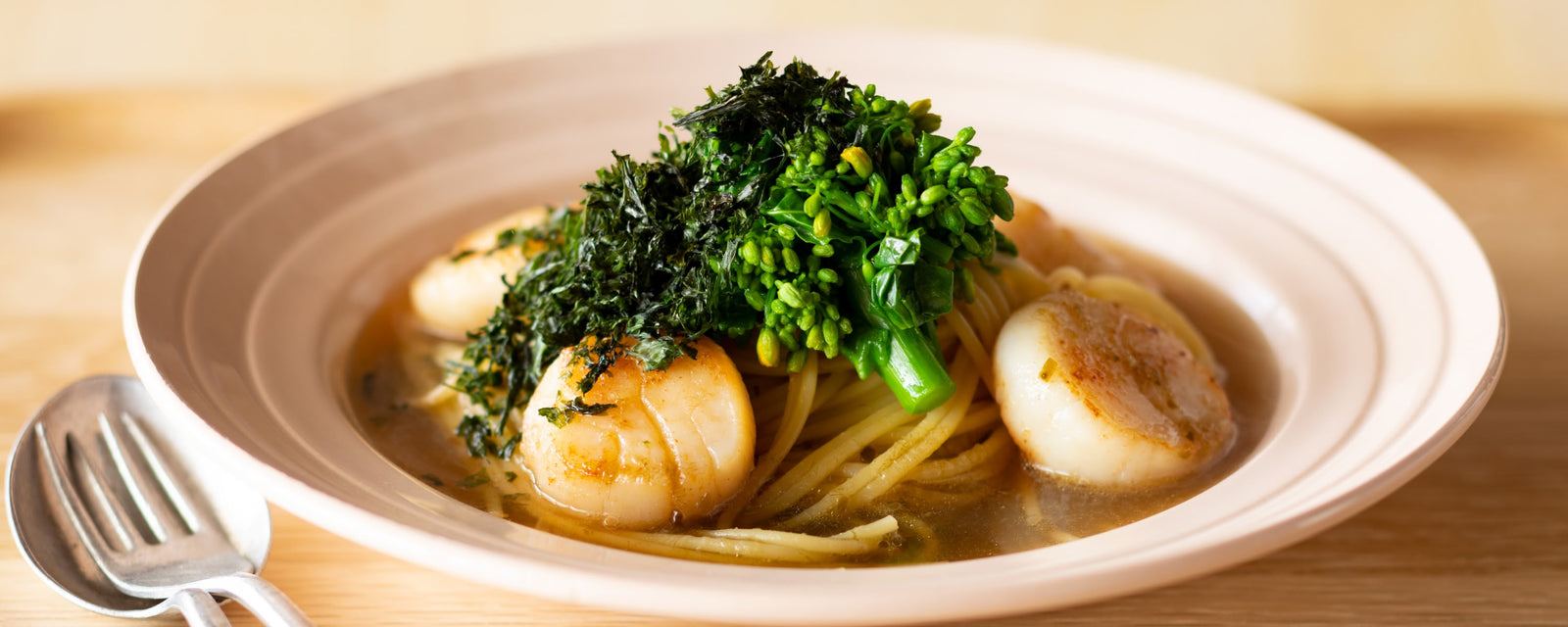 Spaghetti in light umami dashi broth topped with seared scallops, canola flower, and shredded nori
